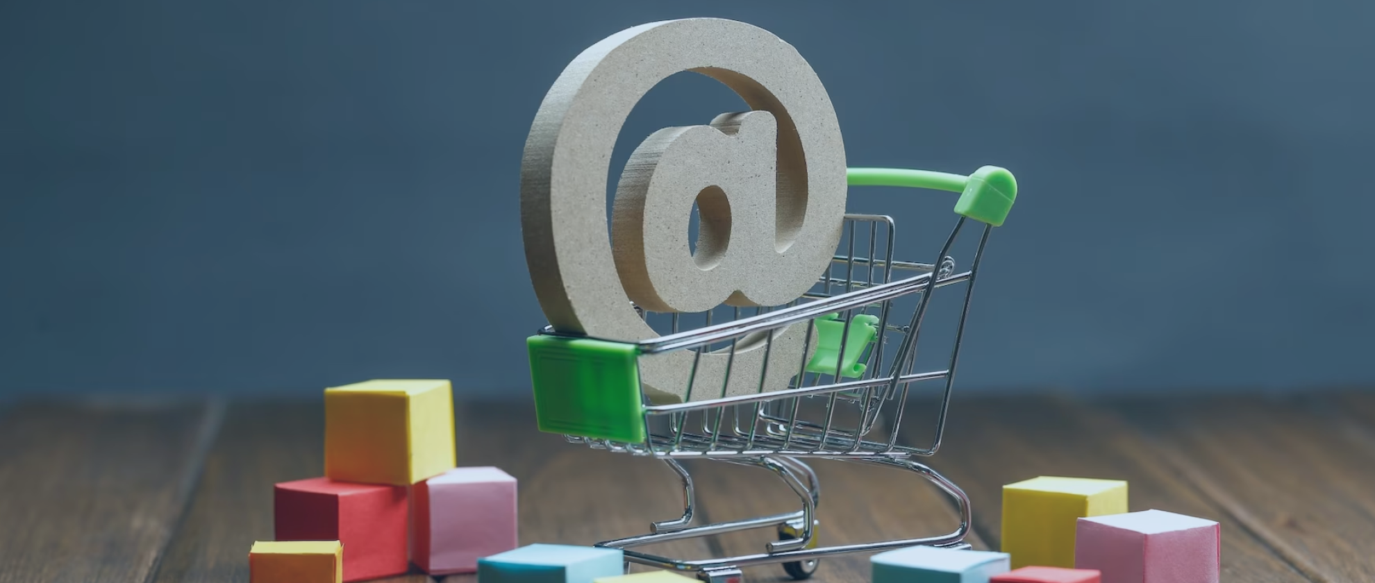 A 3D rendering of a tiny shopping cart carrying a 3D '@' glyph surrounded by tiny paper boxes